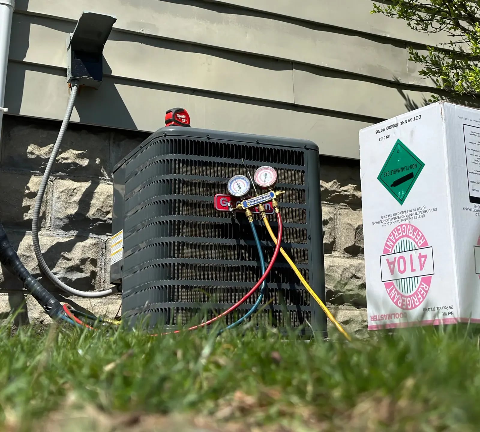 Outdoor condenser with refrigerant gauges connected, next to a refrigerant cylinder