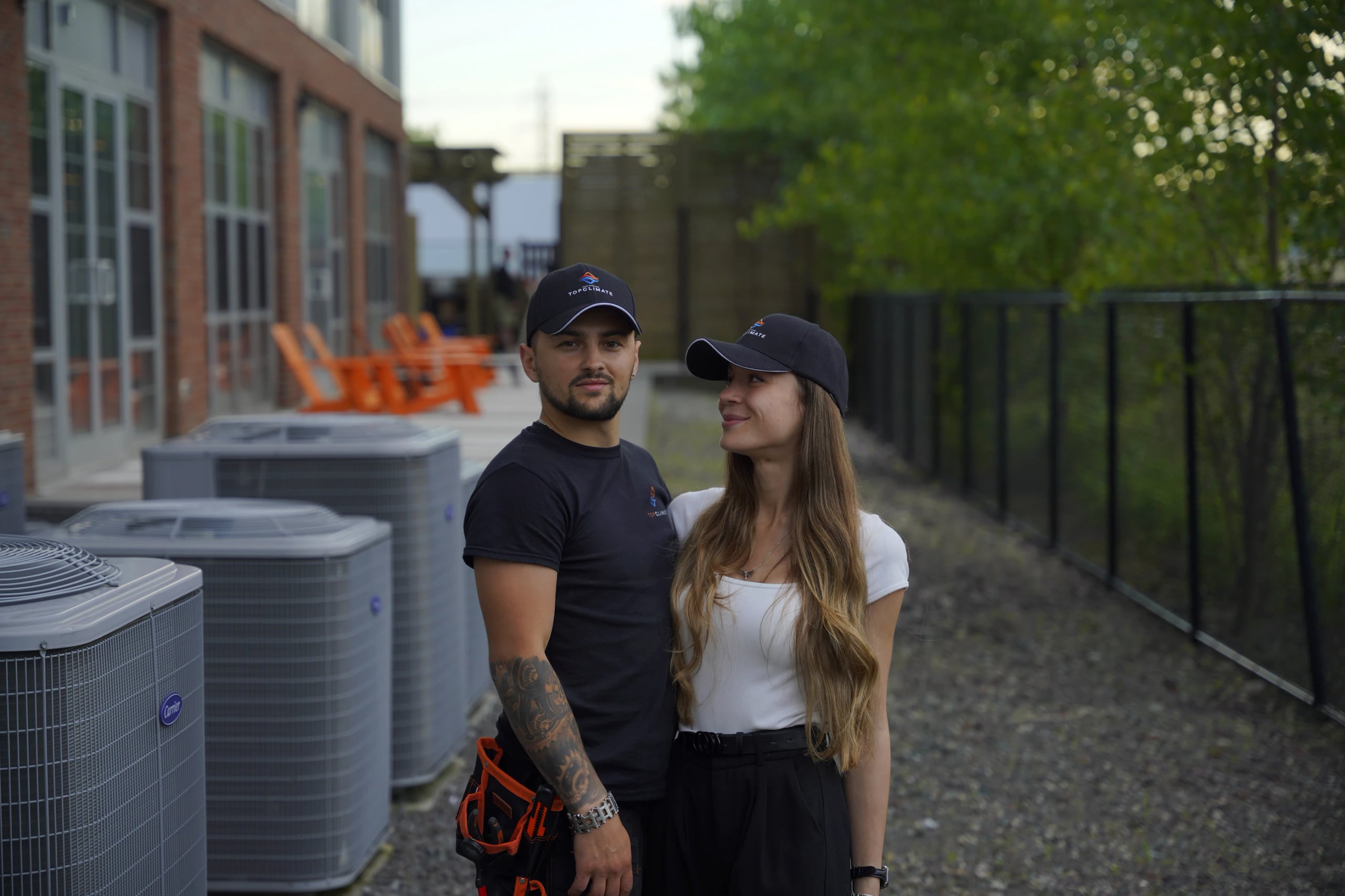 Two Top Climate team members in company caps standing beside a row of outdoor condensing units