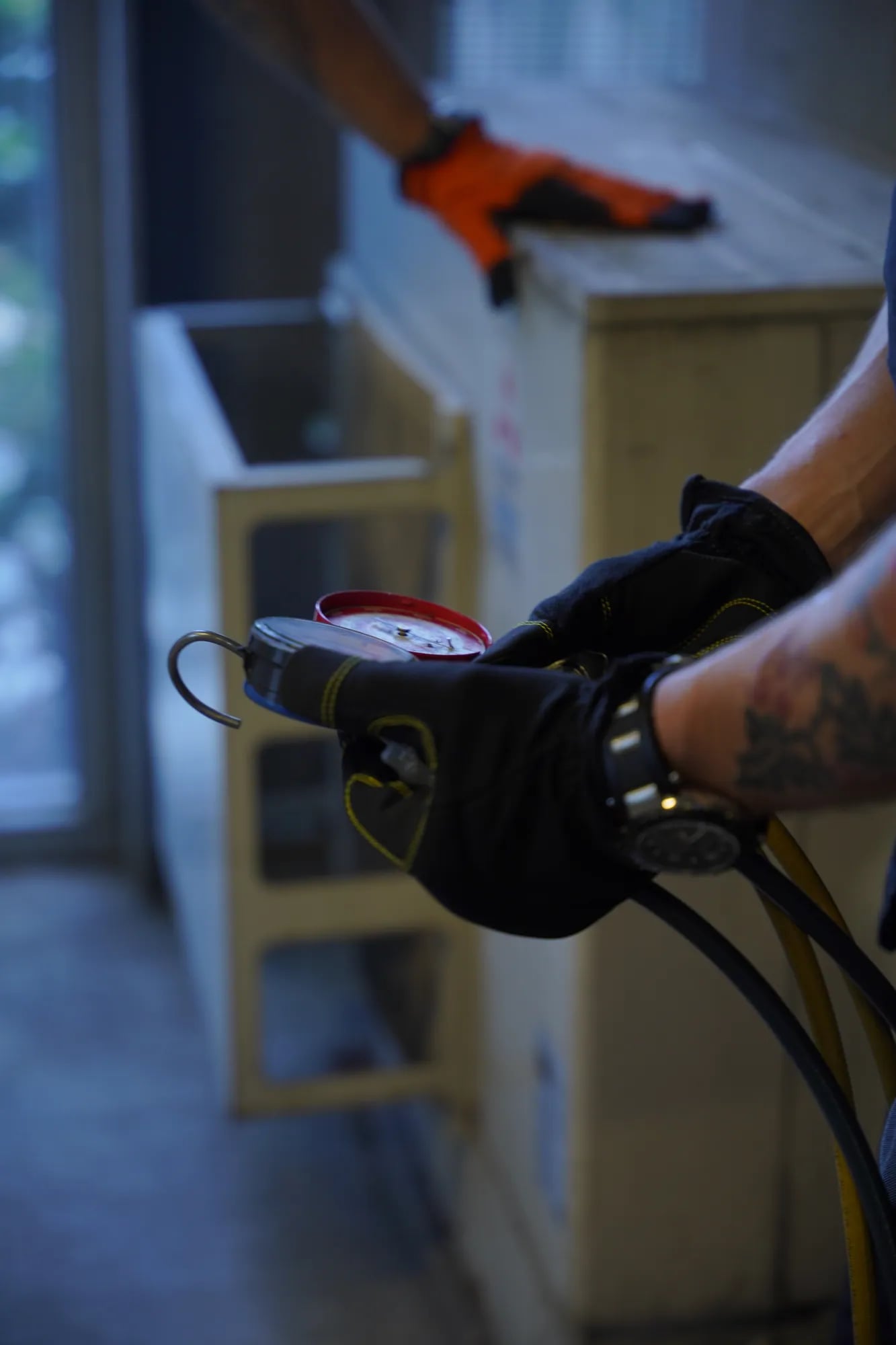 Gloved hands holding refrigerant gauge hoses during a system check