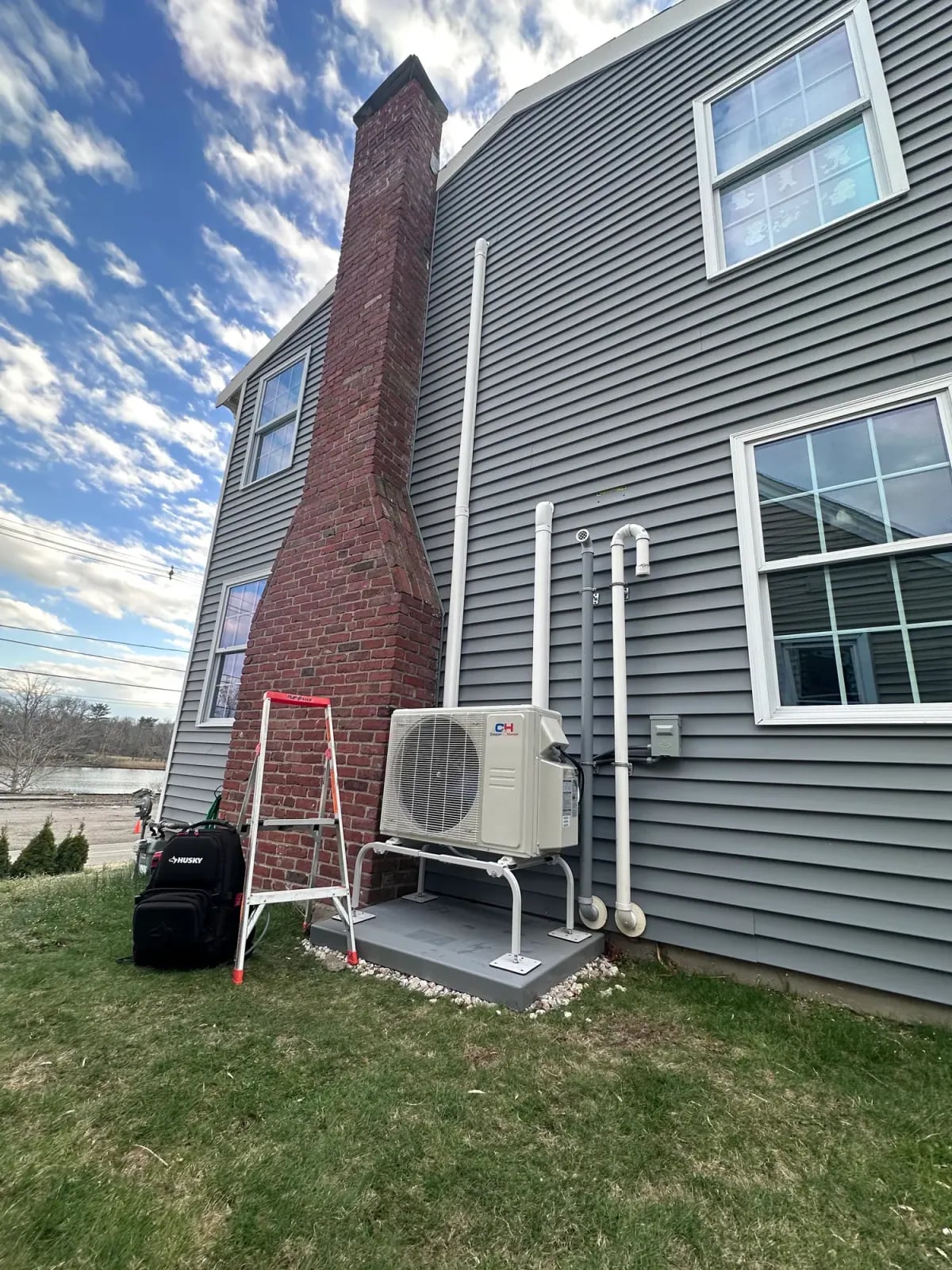 Outdoor heat pump installed on a pad beside a brick chimney