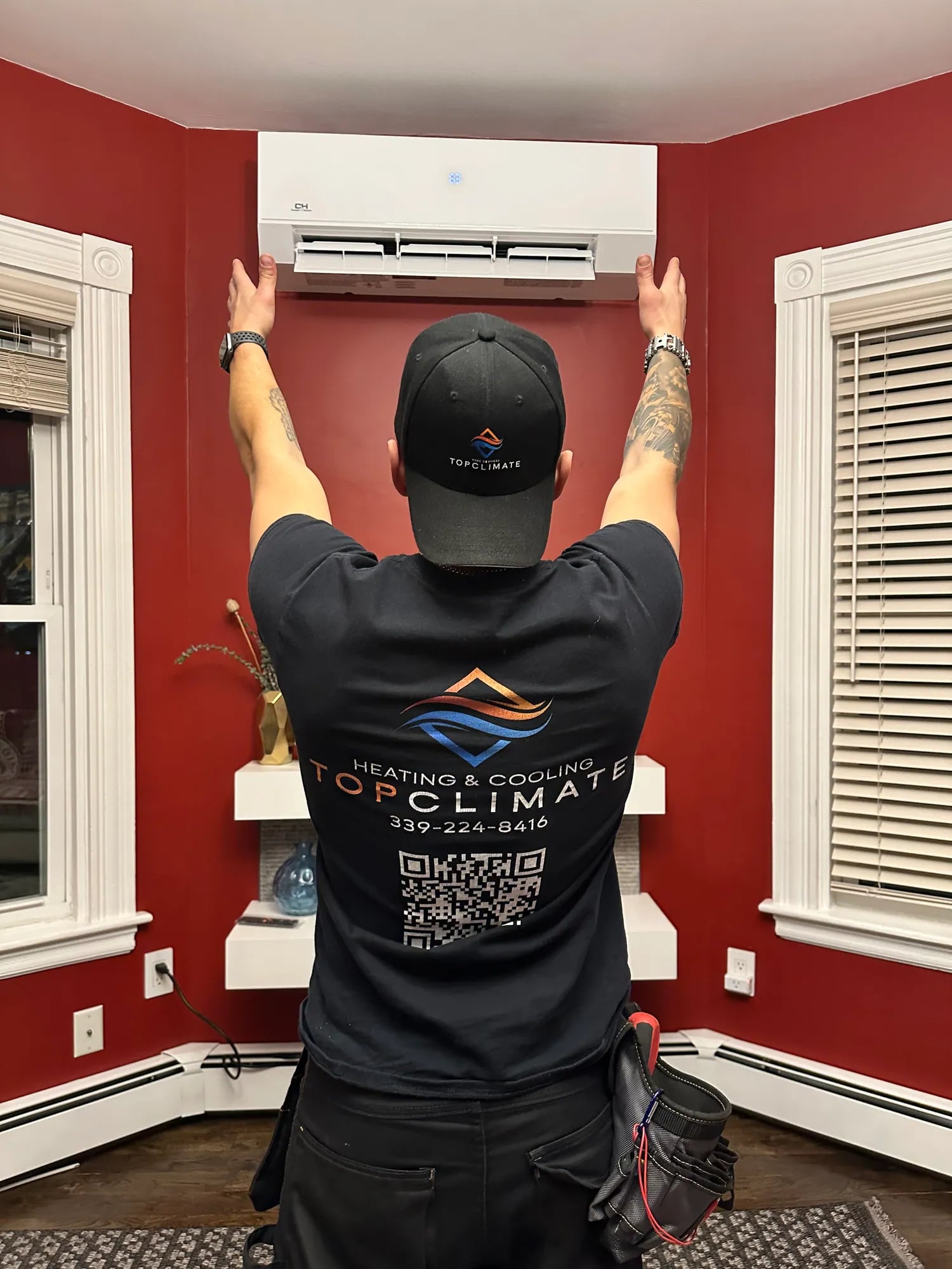 Technician mounting a ductless indoor unit high on the wall of a red room