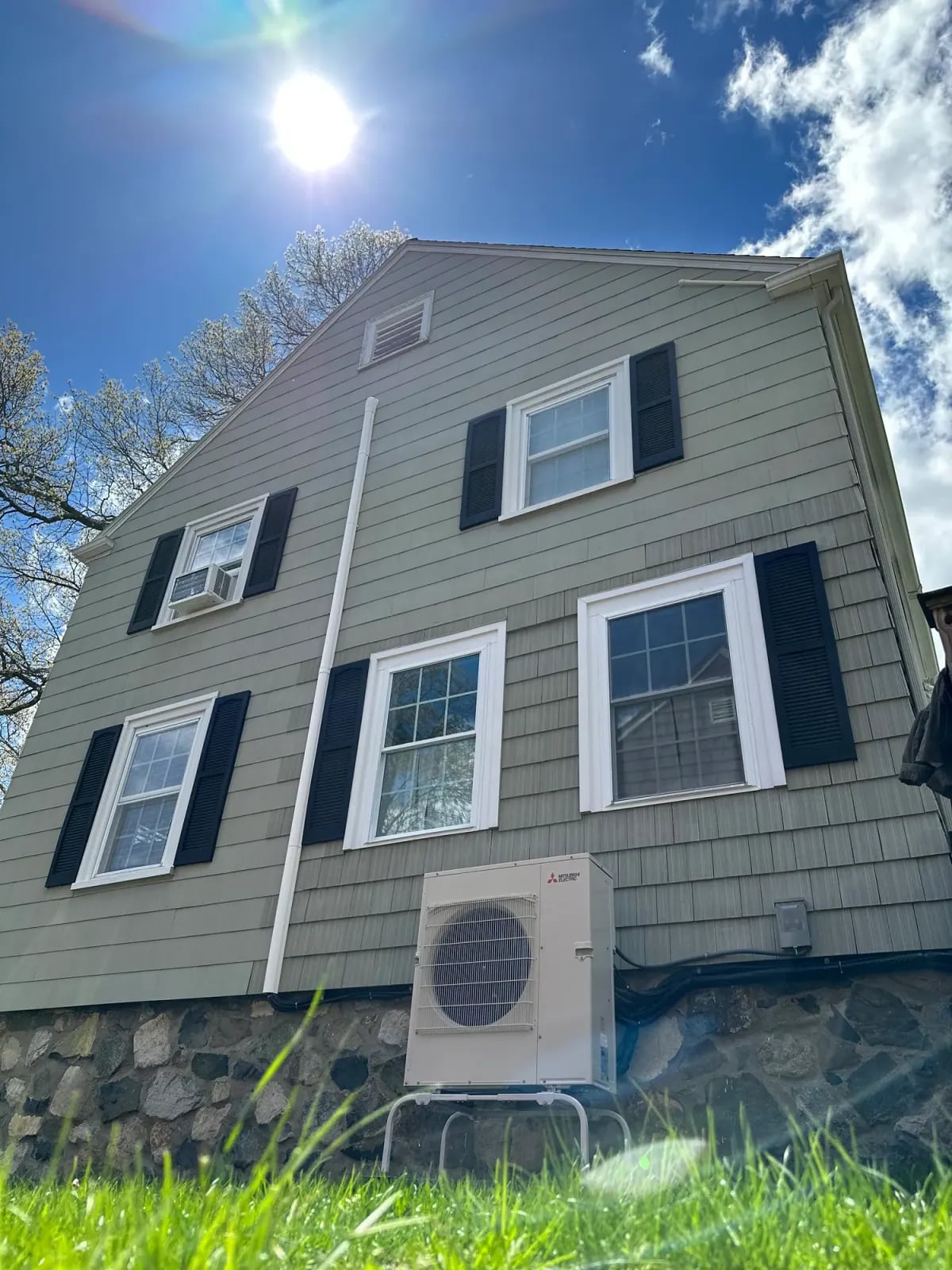 Outdoor mini-split condenser mounted on the wall of a gray clapboard house