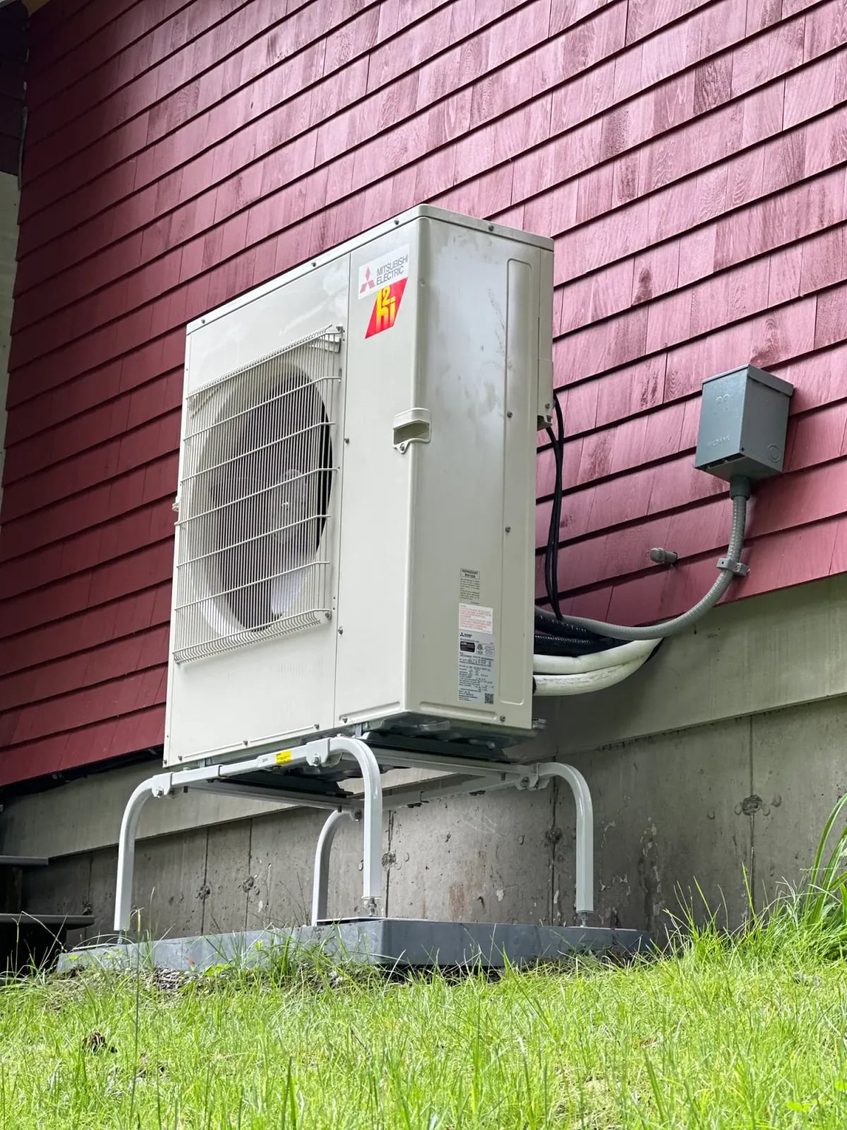 Outdoor heat pump on a stand against a red clapboard wall