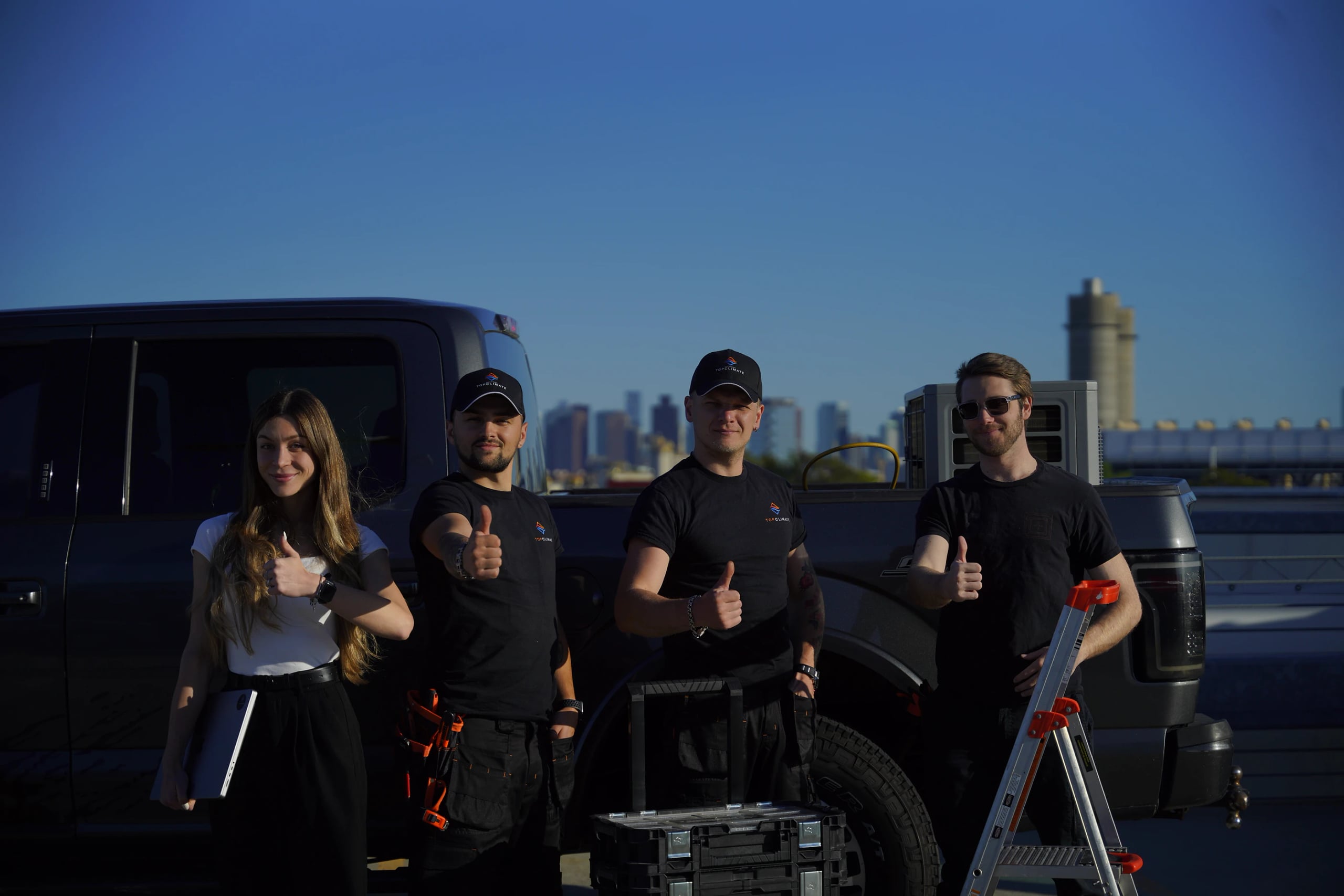Four members of the Top Climate team giving a thumbs up in front of a pickup truck, with the city skyline behind