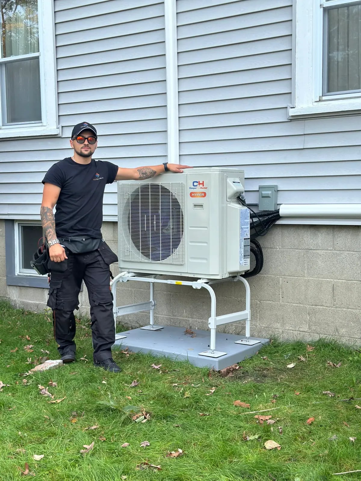 Top Climate technician standing beside a new outdoor heat pump mounted on a stand